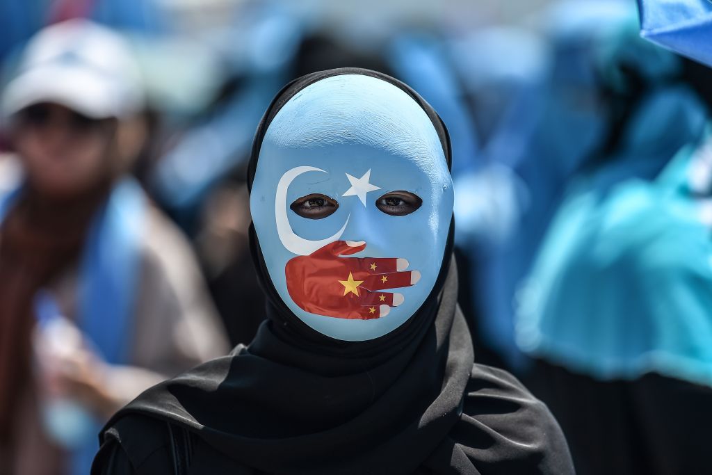 Một người biểu tình đeo mặt nạ sơn màu cờ của Đông Turkestan và tay mang màu cờ Trung Cộng tham dự cuộc biểu tình của những người ủng hộ phần lớn là người Hồi giáo thiểu số Duy Ngô Nhĩ và người theo chủ nghĩa dân tộc Thổ Nhĩ Kỳ để tố cáo Trung Cộng đối xử với người Hồi giáo Duy Ngô Nhĩ, ở phía trước của lãnh sự quán Trung Quốc tại Istanbul vào ngày 5/7/2018. (Ảnh: Ozan Kose/AFP/Getty Images qua The Epoch Times)
