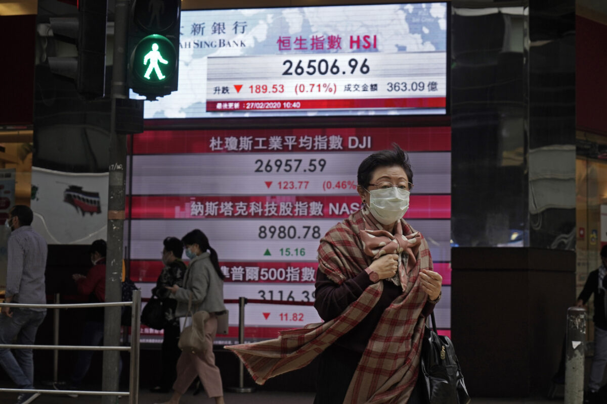 Một phụ nữ đi ngang qua bảng điện tử hiển thị chỉ số cổ phiếu Hồng Kông bên ngoài một ngân hàng địa phương ở Hồng Kông vào ngày 27/2/2020. (Ảnh: Kin Cheung/AP qua The Epoch Times)