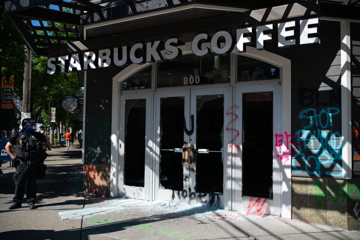 Một sĩ quan cảnh sát vẫn đứng theo dõi sau khi những kẻ bạo loạn đập vỡ cửa sổ và phá hoại một cửa hàng Starbucks, ở Seattle, Wash., vào ngày 25/7/2020. (Ảnh David Ryder / Getty Images)