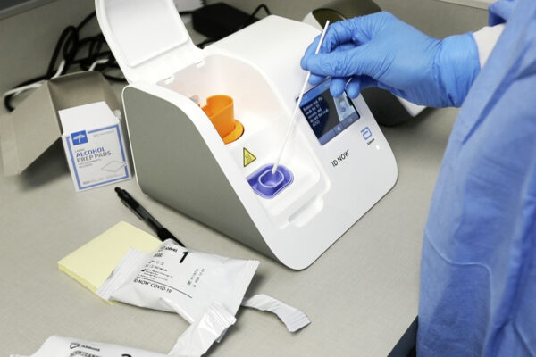Kỹ thuật viên phòng thí nghiệm nhúng mẫu xét nghiệm vào máy kit Abbott Laboratories ID Now tại Trung tâm Y tế Detroit ở Detroit vào ngày 10 tháng 4 năm 2020. (Ảnh Carlos Osorio / AP)