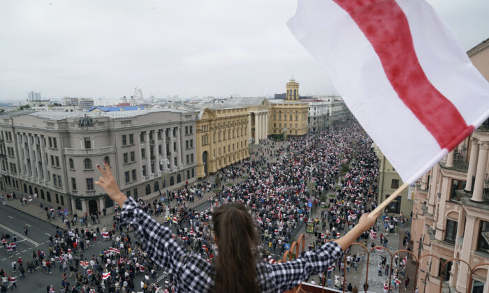 Một phụ nữ vẫy quốc kỳ Belarus cũ đứng trên mái nhà khi những người ủng hộ phe đối lập Belarus diễu hành tới Quảng trường Độc lập ở Minsk, Belarus, vào ngày 3/8/2020. (Ảnh: Evgeniy Maloletka/AP qua The Epoch Times)