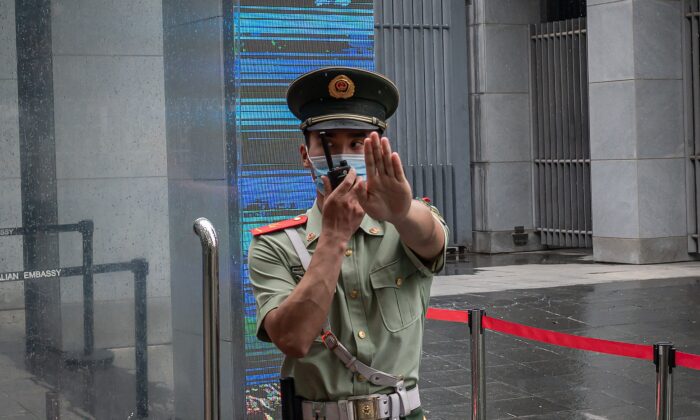 Một sĩ quan cảnh sát Trung Quốc ra hiệu và nói qua điện đàm khi đang đứng tại cổng vào của Đại sứ quán Úc ở Bắc Kinh vào ngày 9/7/2020. (Ảnh Nicolas Asfouri / AFP qua Getty Images)