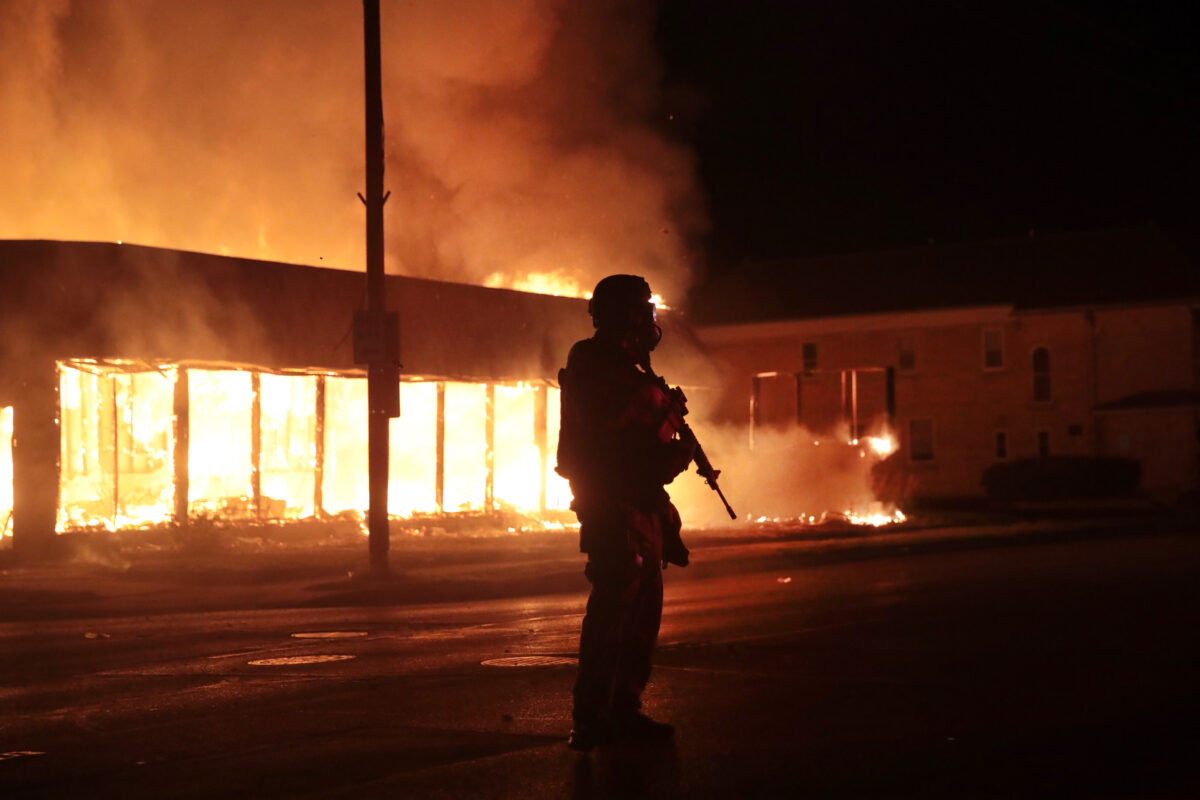 Một sĩ quan cảnh sát đứng gác trước một cơ sở kinh doanh đang bốc cháy trong đêm bạo loạn thứ hai ở Kenosha, Wisconsin, vào ngày 24 tháng 8 năm 2020. (Ảnh: Scott Olson/Getty qua The Epoch Times)
