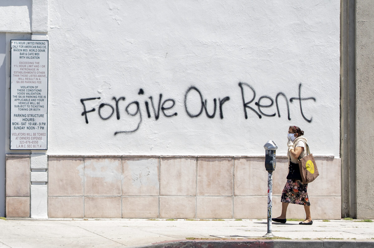 Một phụ nữ đeo khẩu trang đi ngang qua bức tường có hình vẽ graffiti cầu xin sự xoá nợ tiền thuê nhà trong bối cảnh đại dịch COVID-19, ở Los Angeles vào ngày 1/5/2020. (Ảnh Valerie Macon / AFP qua Getty Images)