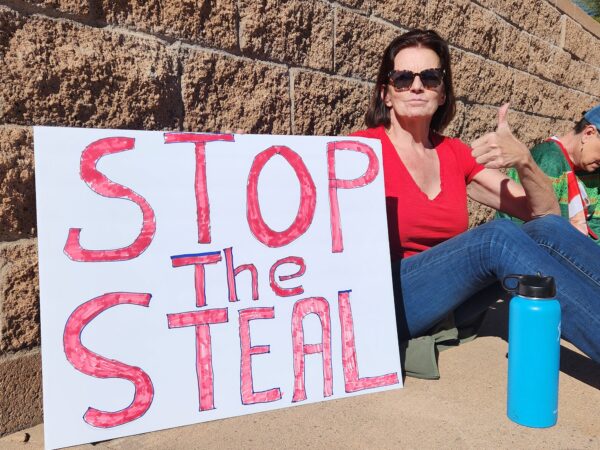 Bà Anne Howell ở Phoenix cầm một tấm biển tuyên bố quan điểm của bà về cuộc bầu cử giữa kỳ ở Arizona tại một cuộc biểu tình “ngồi tại chỗ” cấp cơ sở tại đài tưởng niệm các cựu chiến binh ở Phoenix, hôm 25/11. (Ảnh: Allan Stein/The Epoch Times)