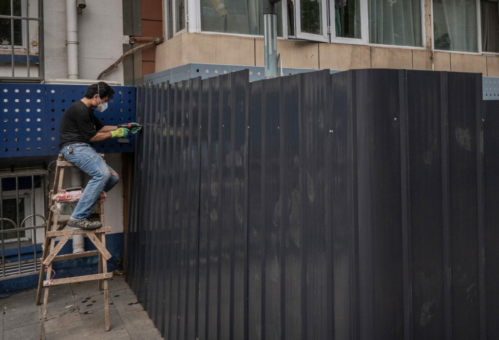 Một nhân viên đang khoan lắp một tấm chắn vào hàng rào ở bên ngoài một căn hộ đã bị phong tỏa sau đợt bùng phát COVID-19 gần đây ở Bắc Kinh, hôm 13/06/2022. (Ảnh: Kevin Frayer/Getty Images)