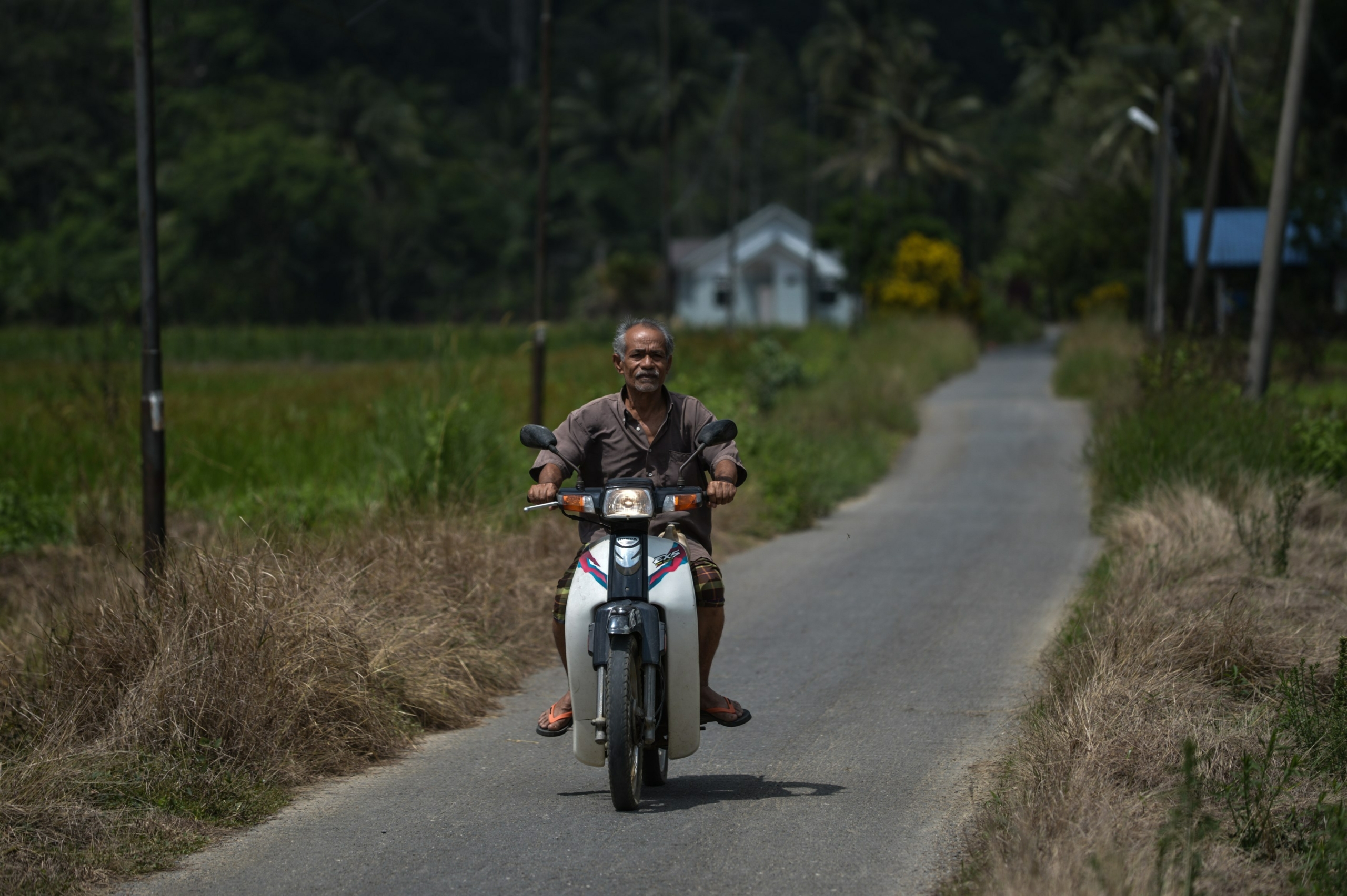 Một người dân làng lái xe máy của mình trên con đường hẹp, thẳng tắp được bao quanh bởi những ngọn đồi và rừng rậm ở Wang Kelian, bang Perlis phía bắc Malaysia, giáp với Thái Lan, vào ngày 27/05/2015. (Ảnh: Mohd Rasfan/AFP qua Getty Images)