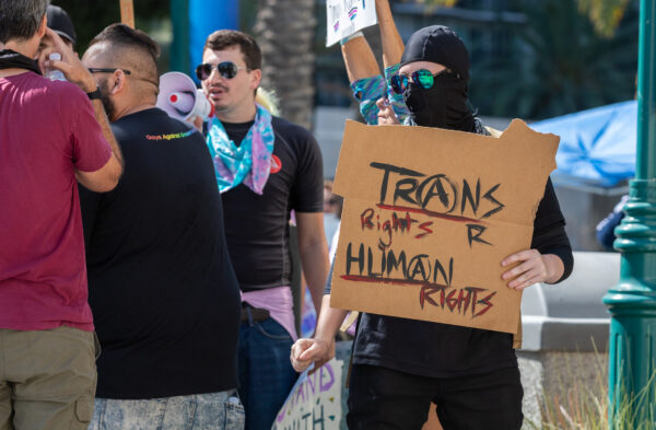 Một nhà hoạt động chuyển giới mặc đồ đen đứng gần những người biểu tình chuyển giới ở Anaheim, California, hôm 08/10/2022. (Ảnh: John Fredricks/The Epoch Times)