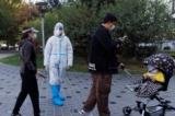 Một nhân viên phòng chống đại dịch mặc bộ đồ bảo hộ trong lúc người dân xếp hàng để lấy mẫu xét nghiệm dịch tỵ hầu tại một quầy xét nghiệm ở Bắc Kinh hôm 03/11/2022. (Ảnh: Thomas Peter/Reuters)