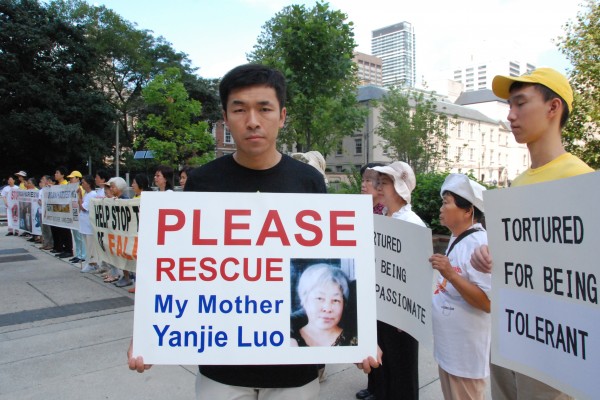 Anh Phạm Văn Thác (Wenta Fan) cầm một tấm biểu ngữ có chân dung của mẹ mình, bà Lạc Diễm Kiệt (Yanjie Luo), người đã bị kết án 13 năm tù ở Trung Quốc vì tu luyện Pháp Luân Công vào năm 2011, bên ngoài Tòa thị chính Toronto vào ngày 25/08/2016. Anh Phạm là một trong số các học viên Pháp Luân Công tại sự kiện thỉnh cầu Thủ tướng Justin Trudeau giúp chấm dứt cuộc bức hại đối với môn tu luyện tinh thần của họ ở Trung Quốc và tìm cách trả tự do cho 12 thân nhân của công dân Canada bị bỏ tù ở Trung Quốc vì tu luyện Pháp Luân Công. (Ảnh: Yi Ling/The Epoch Times)