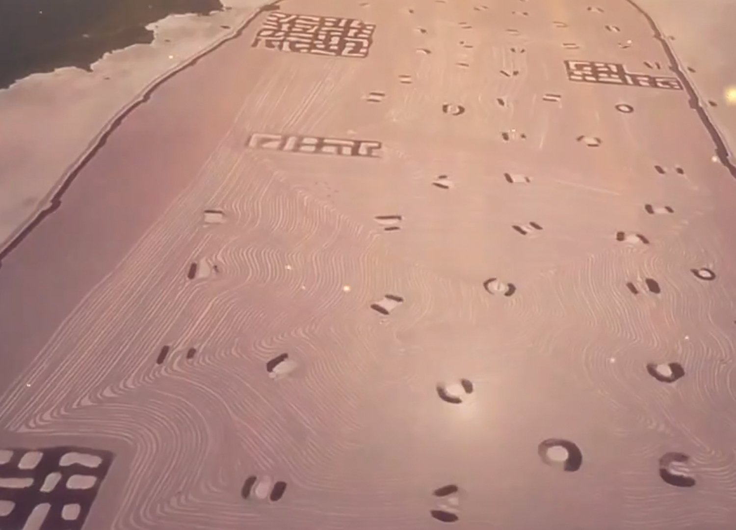 Trong cát vàng của lòng sông có một vùng hình chữ nhật màu đỏ nhạt. Dường như có rất nhiều hoa văn trông giống như ký tự và ký hiệu, có lồi có lõm, rộng khoảng 1.55 km vuông, lớn gấp khoảng hai lần Tử Cấm Thành ở Bắc Kinh. (Ảnh chụp màn hình video Bí ẩn chưa có lời giải)