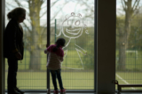 Một bé gái đang vẽ chính mình trên cửa sổ trường học khi con của các nhân viên chủ chốt tham gia các hoạt động của trường tại Trường tiểu học Oldfield Brow ở Altrincham, Anh, vào ngày 08/04/2020. (Ảnh: Christopher Furlong/Getty Images)