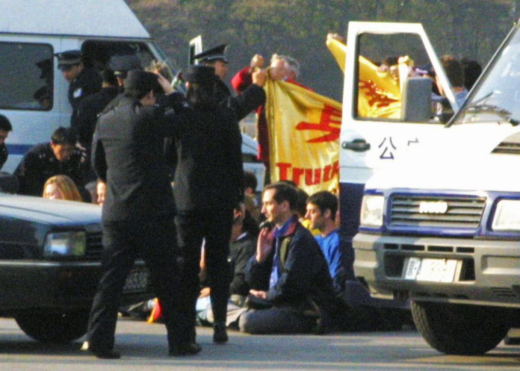 Nhiều học viên phương Tây bị công an Trung Quốc và xe công an bao vây ở Quảng trường Thiên An Môn sau khi giương một tấm biểu ngữ Pháp Luân Công trên Quảng trường Thiên An Môn hôm 20/11/2001. Nhóm này sau đó đã bị công an giải đi và giam giữ. (Ảnh: AP Photo/Ng Han Guan)