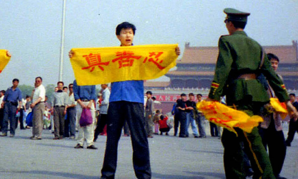 Một sĩ quan công an Trung Quốc tiếp cận một học viên Pháp Luân Công tại Quảng trường Thiên An Môn ở Bắc Kinh khi anh cầm một tấm biểu ngữ có các Hán tự “Chân, Thiện, Nhẫn”, là những nguyên lý cốt lõi của Pháp Luân Công. (Ảnh: Đăng dưới sự cho phép của Minghui.org)