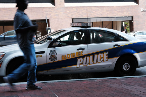 Một người đi ngang qua xe cảnh sát hôm 28/07/2019 tại Baltimore, Maryland. Baltimore có vấn đề tội phạm dai dẳng và có một trong những tỷ lệ sát nhân cao nhất cả nước đối với một thành phố ở bất kỳ quy mô nào. (Ảnh: Spencer Platt/Getty Images)