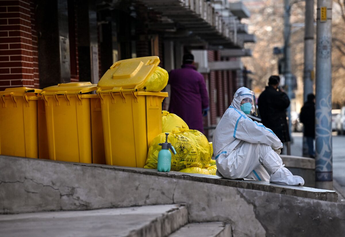 Một nhân viên mặc đồ bảo hộ cá nhân (PPE) ngồi cạnh bãi rác thải bên ngoài một phòng khám sốt giữa đại dịch COVID-19 ở Bắc Kinh hôm 19/12/2022. (Ảnh: Noel Celis/AFP qua Getty Images)