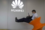 Một người đàn ông đeo khẩu trang ngồi gần logo cửa hàng Huawei ở Bắc Kinh, Trung Quốc, vào ngày 31/07/2020. (Ảnh: Ng Han Guan/Ảnh AP)