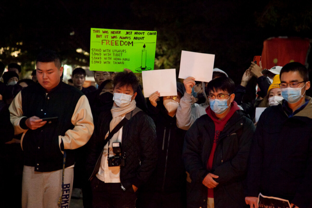 Những người biểu tình cầm biểu ngữ và giấy trắng tại Cổng Sather của UC Berkeley hôm 28/11/2022. (Ảnh: Lear Zhou/The Epoch Times)