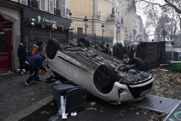 Người dân đi qua những chiếc xe hơi bị lật ngửa trong các cuộc đụng độ sau cuộc biểu tình của các thành viên cộng đồng người Kurd tại Quảng trường Cộng Hòa ở Paris hôm 24/12/2022. (Ảnh: Julien de Rosa/AFP qua Getty Images)