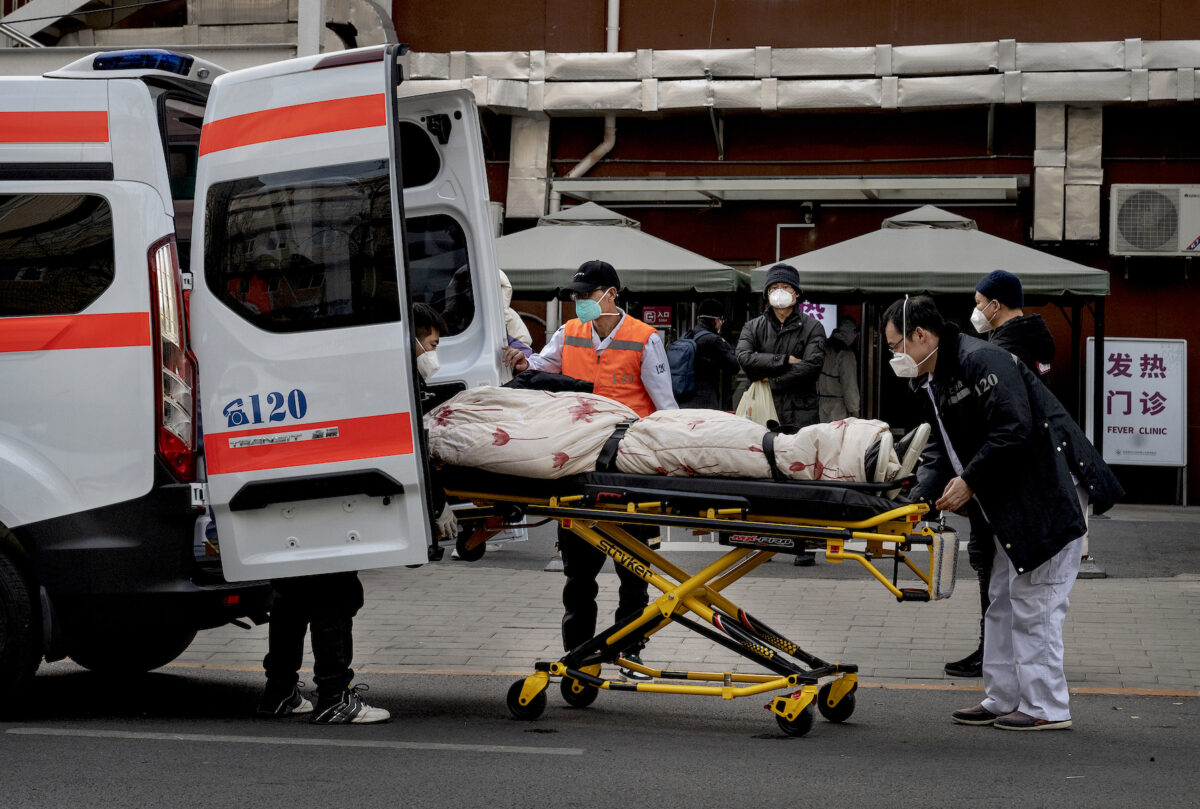 Tài xế xe cứu thương đưa một bệnh nhân rời khỏi xe, bên ngoài một phòng khám điều trị bệnh nhân COVID-19 ở Bắc Kinh hôm 21/12/2022. (Ảnh: Kevin Frayer/Getty Images)