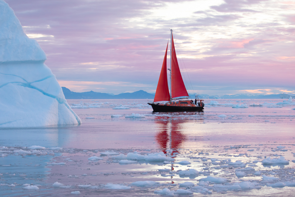 Một chiếc thuyền buồm nhỏ màu đỏ lướt giữa những tảng băng trôi từ Sông băng Disko Bay, Greenland. (Ảnh: Kertu/Shutterstock)