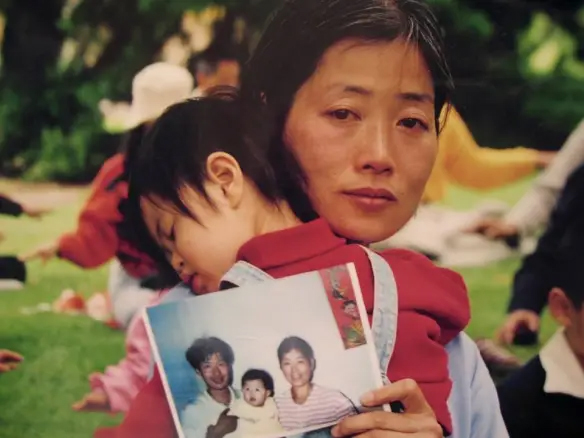 Cô Đới Chí Trân (Jane Dai) cùng con gái, bé Trần Pháp Độ (Chen Fadu), cầm bức ảnh gia đình trước khi cha của bé Pháp Độ, anh Trần Thừa Dũng (Chen Chengyong), bị tra tấn đến tử vong vì tu luyện Pháp Luân Công. (Ảnh: Mimi Li/The Epoch Times)