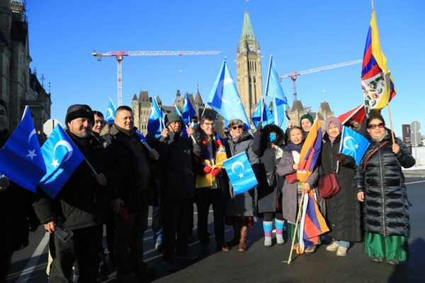 Nghị sĩ Đảng Bảo Thủ Garnett Genuis (Giữa) chụp ảnh cùng những người biểu tình Duy Ngô Nhĩ và Tây Tạng khi những người này tập hợp trước Khu phía Tây trên Đồi Quốc hội để ủng hộ dự luật cấm thu hoạch nội tạng cưỡng bức, tại Ottawa hôm 14/12/2022. (Ảnh: Jian Ren/The Epoch Times)