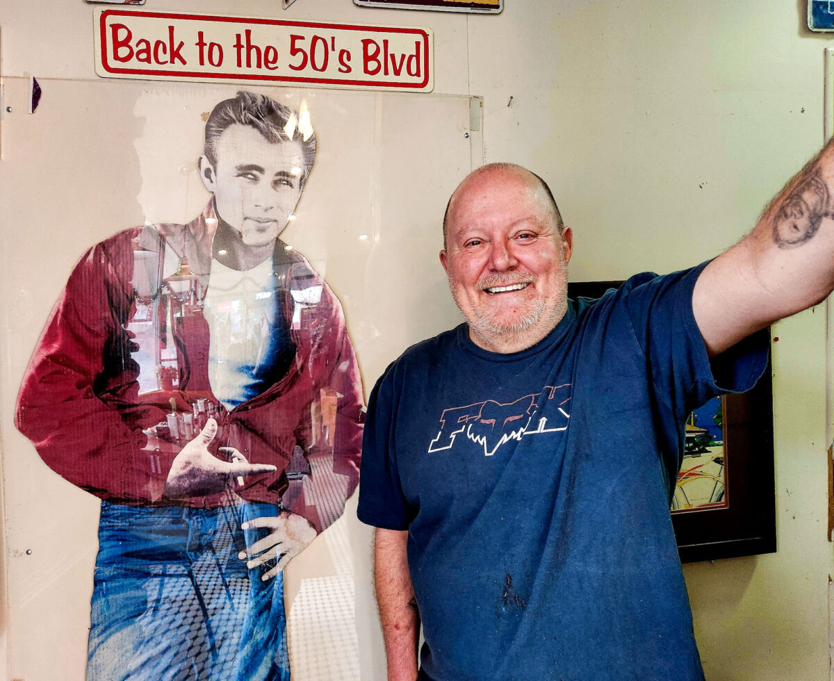 Ông chủ Jeff Pruett của nhà hàng Route 66 đứng cạnh bức ảnh mang tính biểu tượng của tài tử James Dean trước khi nhiều thực khách đến dùng bữa trưa hôm 07/12/2022. (Allan Stein/The Epoch Times)