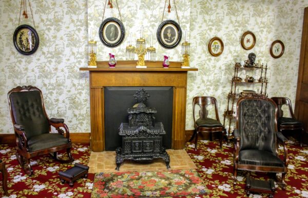 Tuy phong cách Victorian và những phong cách thiết kế nội thất phổ biến khác của thế kỷ 19 thể hiện ở chiếc thảm hoa, giấy dán tường, và phần bài trí cửa sổ trong phòng tiếp khách phía trước nhà, nhưng tính thiết thực lại thể hiện rõ qua những chiếc ghế lông ngựa dệt, được chọn vì độ bền chắc và dễ bọc phần ghế ngồi có khung bằng gỗ. Chiếc lò sưởi đốt củi Temple Parlor thiết kế tinh xảo là một bản sao của phiên bản gốc, hiện được trưng bày tại bảo tàng Henry Ford Museum of Innovation tại thành phố Dearborn, tiểu bang Michigan. Chiếc lò sưởi này có công dụng để sưởi ấm, đồng thời cũng là một vật dụng trang trí trong phòng. Bức ảnh in thạch bản của Quốc phụ George Washington và phu nhân Martha Washington khoảng thế kỷ 19 đặt ở một vị trí trang trọng phía trên chiếc lò sưởi. (Ảnh: Được đăng dưới sự cho phép của Cục Công viên Quốc gia)