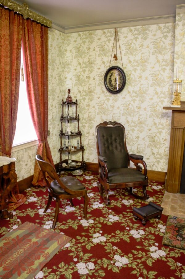 Hiện nay, góc này của phần tiền sảnh tại gian phòng tiếp khách được bày biện giống hệt với khi gia đình Tổng thống Abraham Lincoln còn sinh sống tại ngôi nhà này. Chiếc ghế phụ và ghế bập bênh làm bằng gỗ dái ngựa (gỗ mahogany) cũng bọc lông ngựa dệt giống với tất cả những chiếc ghế bọc khác trong nhà, trong khi đó chiếc kệ gỗ ở góc nhà (một kệ sách có dạng bậc thang) trưng bày với những “món đồ trang trí cổ xưa,” hay những thứ mà hiện nay chúng ta gọi là vật dụng trang trí linh tinh. Treo trên tường là một chiếc hộp bóng chứa một tác phẩm nghệ thuật trưng bày những lọn tóc thật, đây cũng là một vật dụng phổ biến khác của thế kỷ 19. (Ảnh: Được đăng dưới sự cho phép của Cục Công viên Quốc gia)