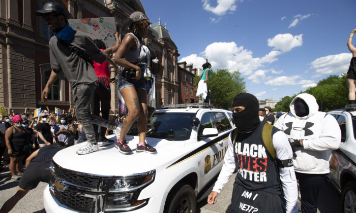 Những người biểu tình nhảy lên nắp một chiếc xe của cảnh sát mật vụ bên ngoài Tòa Bạch Ốc ở Hoa Thịnh Đốn, trong một cuộc biểu tình về việc ông George Floyd bị thiệt mạng, ngày 30/05/2020. (Ảnh: Jose Luis Magana/AFP qua Getty Images)