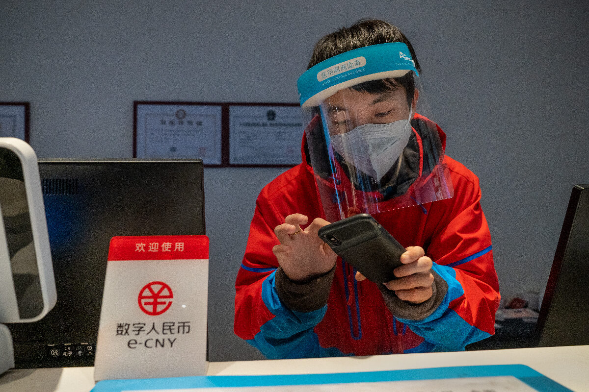 Một nhân viên tại quầy lễ tân của Khách sạn Prince Ski Town kiểm tra điện thoại đằng sau một tấm biển ghi “chấp nhận đồng nhân dân tệ kỹ thuật số (e-CNY)” ở Trương Gia Khẩu, Trung Quốc, vào ngày 04/12/2021. (Ảnh: Andrea Verdelli/Getty Images)