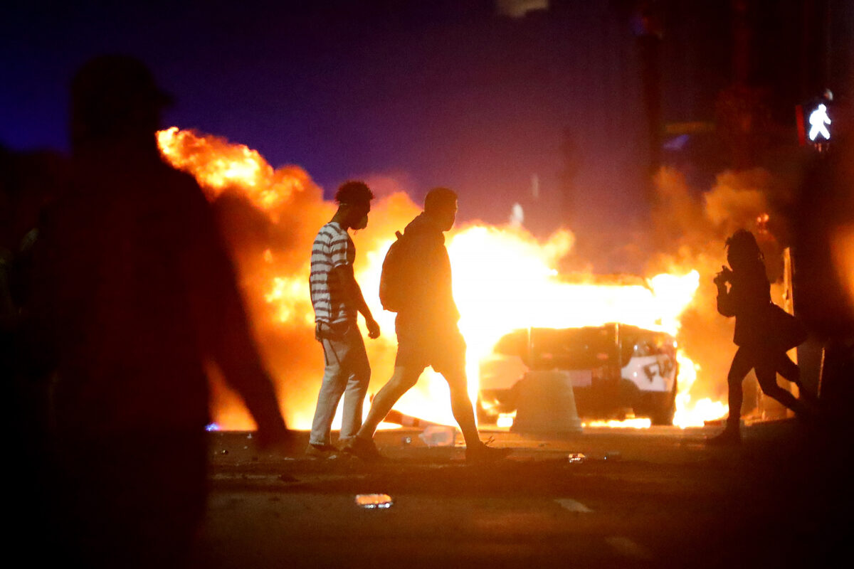 Những người biểu tình đi ngang qua một chiếc xe cảnh sát đã bị phóng hỏa trong một cuộc biểu tình phản ứng trước việc ông George Floyd thiệt mạng ở Boston, Massachusetts, vào ngày 31/05/2020. (Ảnh: Maddie Meyer/Getty Images)