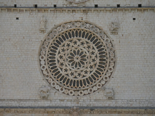 Trên phần tympanum (một mặt tường trang trí bên trên một lối vào, cánh cửa, hay cửa sổ) nằm ở phía trên hai vòm cung nhọn bên ngoài thánh đường này, có một cửa sổ hoa hồng được chạm khắc tinh tế, vốn là các chi tiết trang trí mang nét đặc trưng của kiến trúc Romanesque. Mặt tường trang trí này được bao bên trong một mái hiên theo phong cách Phục Hưng cùng với các bức tường đá lớn màu trắng và các khung cửa sổ hình vòm cung. Khung cửa sổ này thường được gọi là “Con mắt của Chúa” hay “Con mắt của nhà thờ đẹp nhất trên thế giới,” dựa theo lời của tác giả Gualtiero Belucci trong tác phẩm “Assisi, Trái Tim của Thế Giới.” (Ảnh: FillipoPH/Shutterstock)