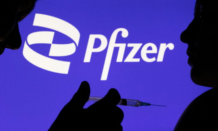 Một người cầm ống chích tạo dáng trước logo Pfizer Inc. vào ngày 11/12/2021. (Ảnh: Dado Ruvic/Reuters)