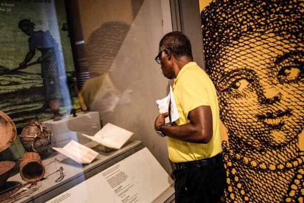 Một vị khách xem một bản thống kê điều tra dân số và bản kiểm chứng của Virginia, trong đó đề cập đến người phụ nữ Phi Châu đầu tiên được ghi nhận đã đến thuộc địa này, tại một khu trưng bày lịch sử ở Williamsburg, Virginia, ngày 19/08/2019. (Ảnh: Brendan Smialowski/AFP qua Getty Images)