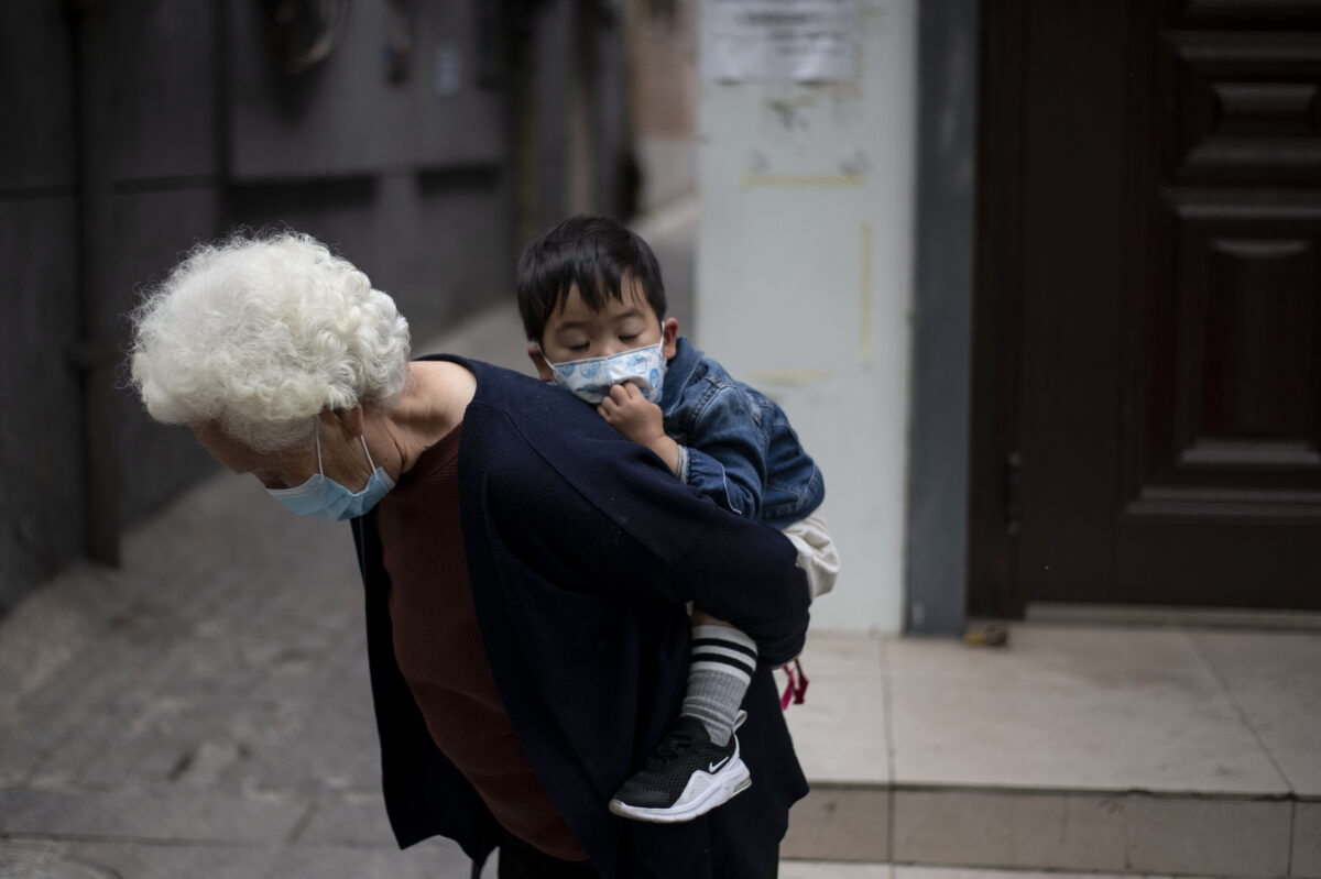 Một người phụ nữ cao tuổi đang cõng một cậu bé dọc theo một con đường tại Bắc Kinh vào ngày 11/05/2020. (Ảnh: Noel Celis/AFP qua Getty Images)