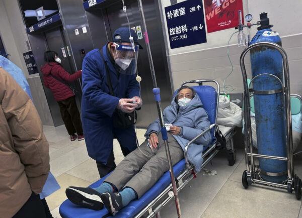 Một người đàn ông đeo khẩu trang khi giúp người thân nằm trên cáng ở hành lang của một bệnh viện đông đúc ở Thượng Hải hôm 14/01/2023. (Ảnh: Kevin Frayer/Getty Images)