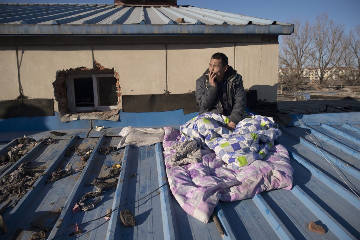 Một công nhân nhập cư bị đuổi khỏi phòng trong một khu nhà dành cho người có thu nhập thấp đang ngồi trên mái nhà nơi anh đang ở, chờ nhận lương trước khi trở về nhà ở miền nam đất nước, tại một làng di cư ở ngoại ô Bắc Kinh, vào ngày 11/12/2017. (Ảnh: Nicolas Asfouri/AFP qua Getty Images)