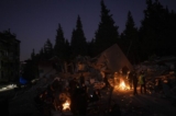 Những người bạn và người thân của gia đình Daghli quây quần bên đống lửa trong khi đội cứu hộ tìm kiếm các thành viên trong gia đình dưới đống đổ nát của một tòa nhà bị phá hủy ở Antakya, đông nam Thổ Nhĩ Kỳ, hôm 15/02/2023. (Ảnh: Bernat Armangue/AP Photo)