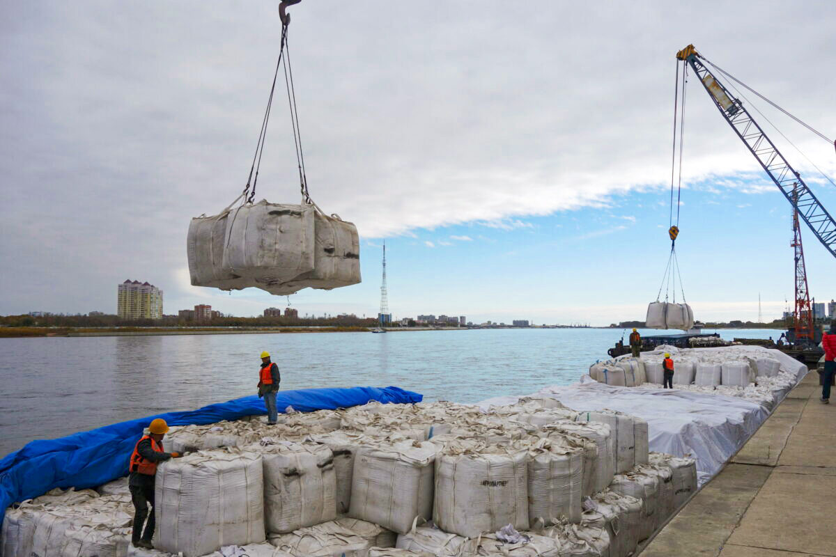 Các công nhân đứng gần một chiếc cần cẩu đang dỡ các bao tải đậu nành nhập cảng từ Nga tại cảng Hắc Hà ở tỉnh Hắc Long Giang, Trung Quốc, vào ngày 10/10/2018. (Ảnh: Stringer/Reuters)