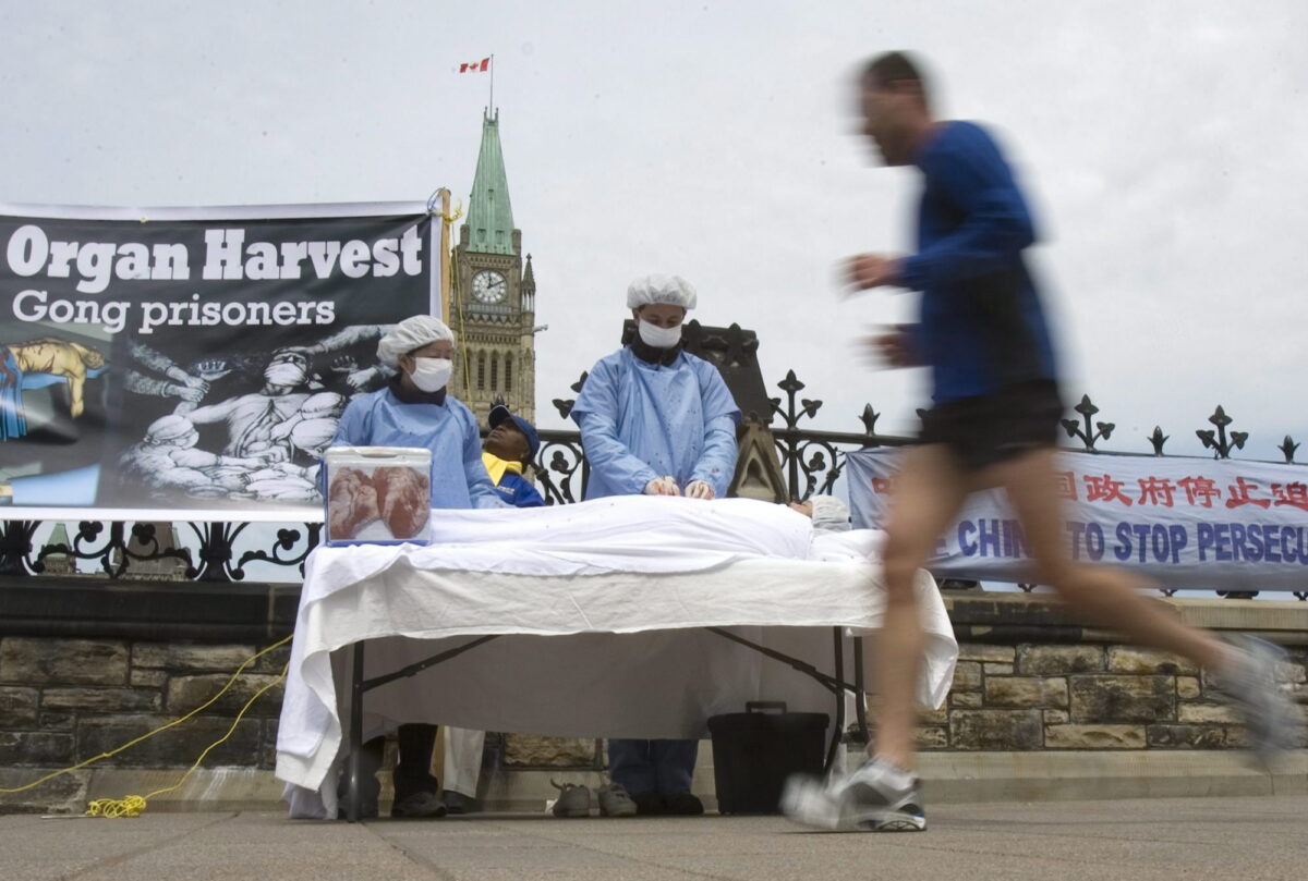 Một người đàn ông chạy bộ ngang qua trong khi các học viên Pháp Luân Công đang diễn lại hành vi cưỡng bức thu hoạch nội tạng như một phần trong cuộc phản kháng của họ đối với ĐCSTQ và cuộc bức hại của đảng này đối với các học viên Pháp Luân Công, tại Capitol Hill ở Ottawa, Canada, vào ngày 02/05/2008. (Ảnh: Tom Hanson/The Canadian Press)