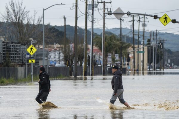 Người dân đi bộ qua vùng nước lũ ở Watsonville, California, hôm 11/03/2023. Thống đốc Gavin Newsom đã tuyên bố tình trạng khẩn cấp ở 34 quận trong những tuần gần đây, và chính phủ Tổng thống Biden đã phê chuẩn tuyên bố thảm họa của tổng thống cho một số khu vực vào sáng thứ Sáu, một hành động sẽ đem lại sự trợ giúp liên bang nhiều hơn. (Ảnh: AP Photo/Nic Coury)