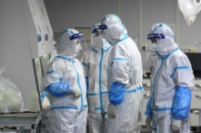 Các kỹ thuật viên phòng thí nghiệm đeo thiết bị bảo vệ cá nhân đang làm việc trên các mẫu bệnh phẩm tầm soát virus COVID-19 tại Phòng thí nghiệm Hỏa Nhãn, một cơ sở xét nghiệm COVID-19, tại Vũ Hán ở tỉnh Hồ Bắc, miền trung Trung Quốc, vào ngày 04/08/2021. (Ảnh: STR/AFP qua Getty Images)