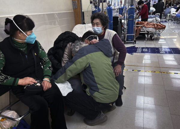 Một người đàn ông ôm người họ hàng lớn tuổi khi ông và những người khác giúp đỡ bà người hiện đang được chăm sóc ở hành lang của phòng cấp cứu đông đúc tại một bệnh viện ở Thượng Hải hôm 14/01/2023. (Ảnh: Kevin Frayer/Getty Images)