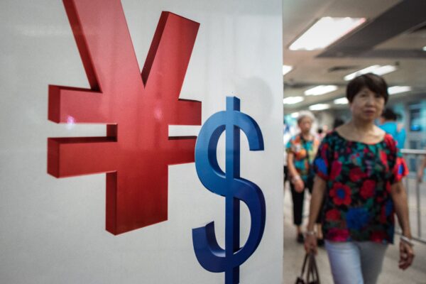 Một người phụ nữ đi ngang qua ký hiệu tiền nhân dân tệ (trái) và USD (phải) ở Hồng Kông hôm 13/08/2015. (Ảnh: Philippe Lopez/AFP qua Getty Images)