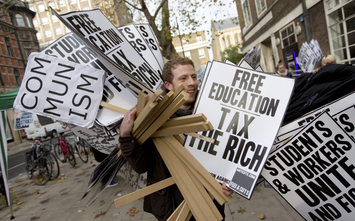 Một người đàn ông mang những tấm bảng ghi “Giáo dục miễn phí. Đánh thuế người giàu” và “Chủ nghĩa cộng sản” trong một bức ảnh tư liệu. (Ảnh: Justin Tallis/AFP qua Getty Images)