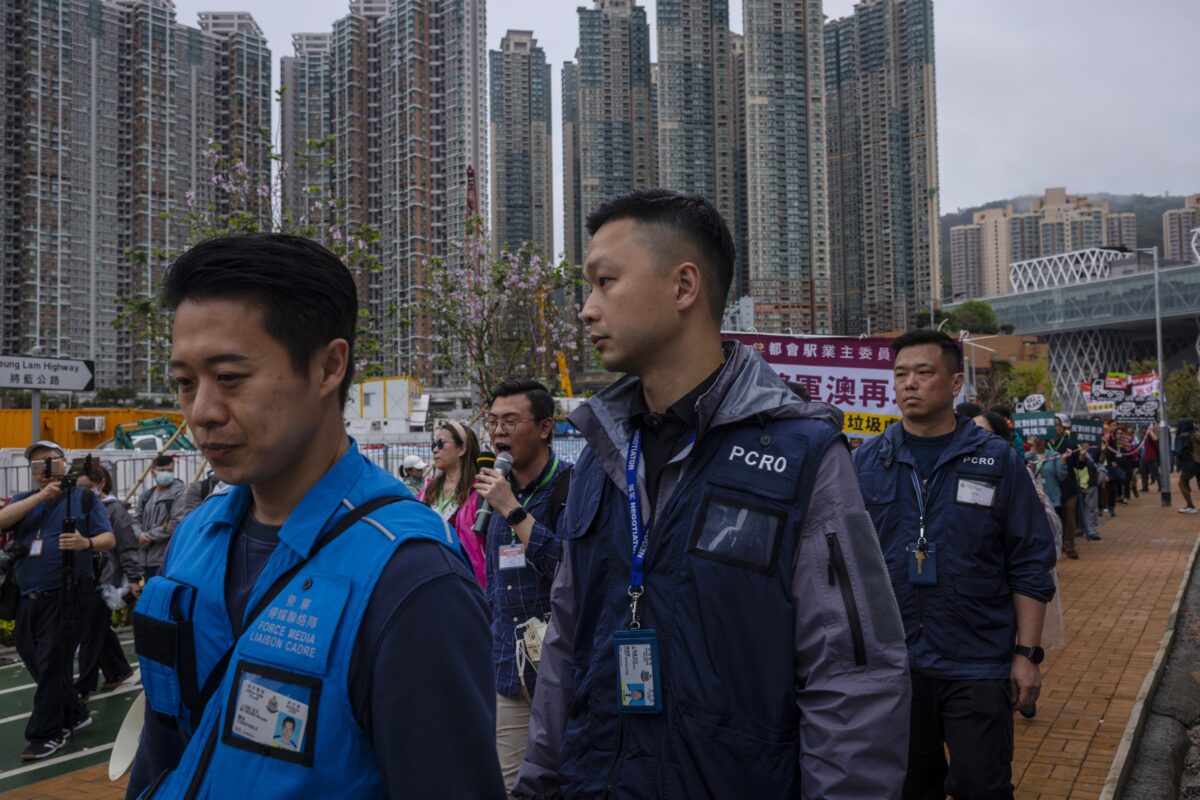 Cảnh sát song hành cùng đoàn người biểu tình đeo thẻ có đánh số đi trong khu vực có rào chắn trong một cuộc biểu tình ở Hồng Kông hôm 26/03/2023. (Ảnh: Louise Delmotte/AP)