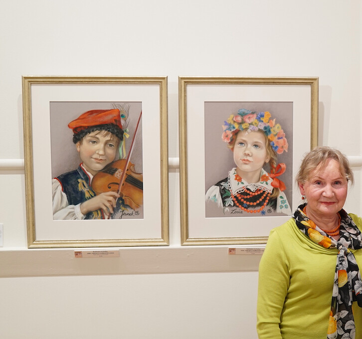 Họa sĩ Barbara Schafer bên cạnh bức tranh bằng phấn màu vẽ các trẻ em Ba Lan trong trang phục truyền thống tại một buổi triển lãm nghệ thuật Ba Lan có nhan đề “Roots” (Nguồn cội) ở Melbourne, nước Úc, năm 2018. (Ảnh: Đăng dưới sự cho phép của bà Barbara Schafer)