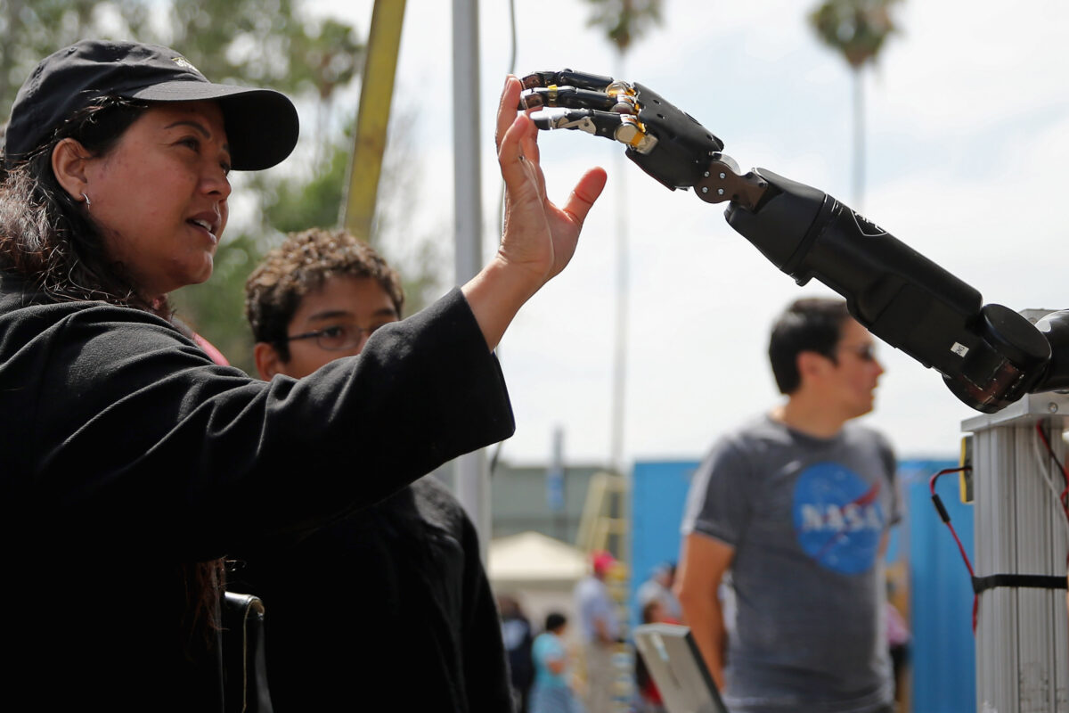 Một người phụ nữ đưa tay để chạm vào cánh tay của người máy do Phòng thí nghiệm Vật lý Ứng dụng của Đại học Johns Hopkins phát triển được trưng bày tại Cơ quan Dự án Nghiên cứu Tân tiến Quốc phòng (DARPA, nhóm nghiên cứu khoa học của Ngũ Giác Đài) tại Triển lãm Thử thách Robotics tại Fairplex ở Pomona, California, hôm 06/06/2015. (Ảnh: Chip Somodevilla/Getty Images)